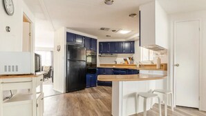 A modern kitchen with a central island, dark blue cabinets, and a stainless steel refrigerator.