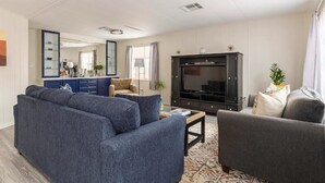 A living room with a grey sofa, a smaller armchair, a TV stand, and a patterned rug.
