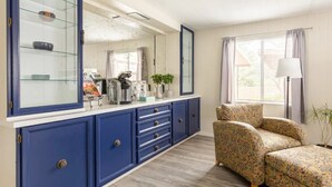 A room with a blue cabinet, a glass display case, a patterned armchair, a lamp, and a window with curtains.