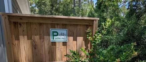 Una caseta de fusta amb un senyal de 'PARKING', aparca-bicis metàl·liques i un petit arbre.