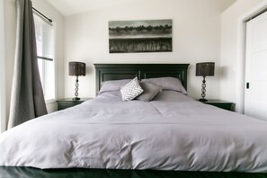 A neatly made bed with a grey and white patterned pillow, two bedside lamps, and a painting of a landscape above the bed.