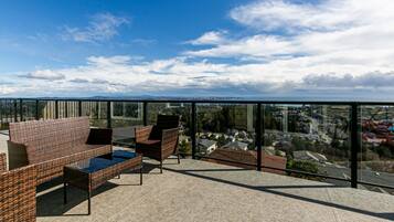 A balcony with wicker furniture and a glass railing overlooking a residential area.