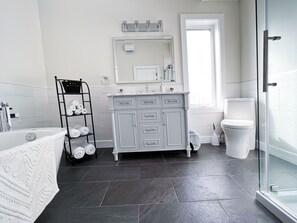 A modern bathroom with a grey vanity, a white bathtub, and a glass shower enclosure.