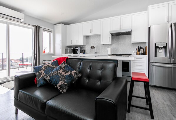 A modern kitchen with white cabinets, stainless steel appliances, and a black leather sofa with patterned cushions.