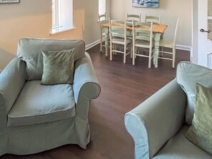 A living room with two light green armchairs, a wooden dining table with chairs, and a painting on the wall.
