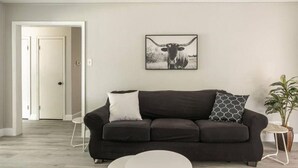A modern living room with a dark sofa, a white coffee table, and a framed picture of a cow on the wall. - Spacious retreat near Dallas for group stays (Garland)