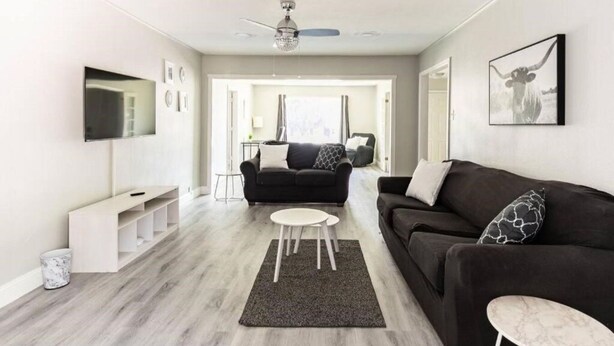 A modern living room with a grey sofa, a black sofa, a white coffee table, and a grey rug. There is a TV mounted on the wall, a ceiling fan, and a framed picture on the wall. - Spacious retreat near Dallas for group stays (Garland)