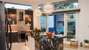 Une cuisine moderne dotée d’un îlot en marbre, d’appareils électroménagers noirs et de luminaires suspendus.