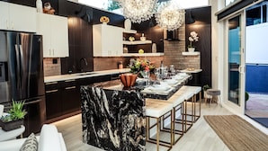 Une cuisine moderne avec des meubles de couleur sombre, un îlot en marbre et des luminaires suspendus.