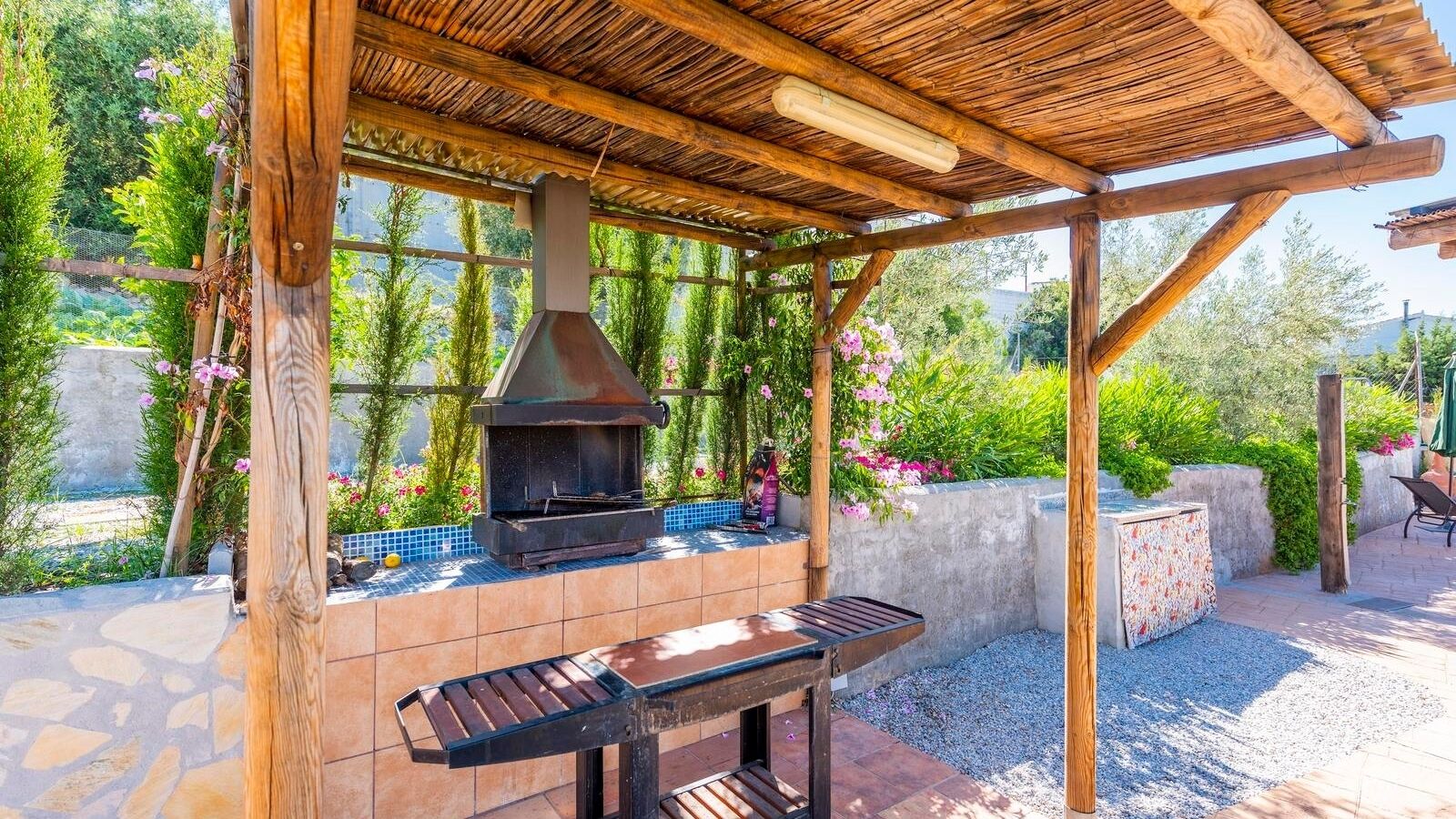An outdoor patio with a built-in grill, a wooden pergola, and a stone-tiled floor.