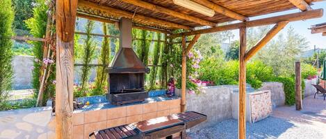 An outdoor patio with a built-in grill, a wooden pergola, and a stone-tiled floor.