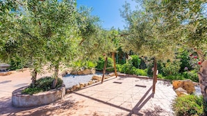 An outdoor patio area with a tiled floor, surrounded by greenery and rocks.
