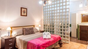 A bedroom with a bed, bedside tables, a nightstand, a window with a view, and a small kitchenette.