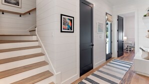 A hallway with white paneled walls, a wooden staircase, and a black door.