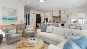 A spacious living room with a large sofa, two armchairs, and a coffee table. A dining area with a table and chairs is visible in the background.