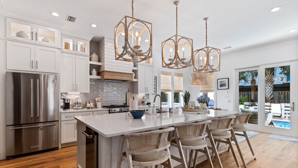 A modern kitchen with white cabinetry, a stainless steel refrigerator, a large island with bar stools, and pendant lighting.