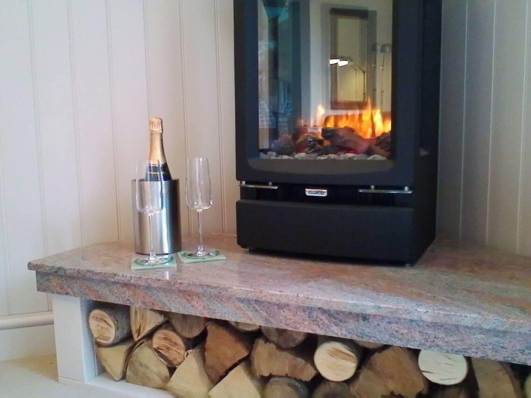 A stone fireplace with a log fire, a bottle of champagne, and two glasses on a marble countertop.