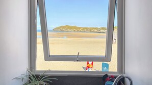 A window view of a beach with a sandy shore, a grassy hill, and a blue sky. - Pennti Treth - UK39455 (Porth, near Newquay)