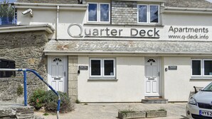A building named 'Quarter Deck Apartments' with a stone facade, two white doors, and a website address. - Pennti Treth - UK39455 (Porth, near Newquay)