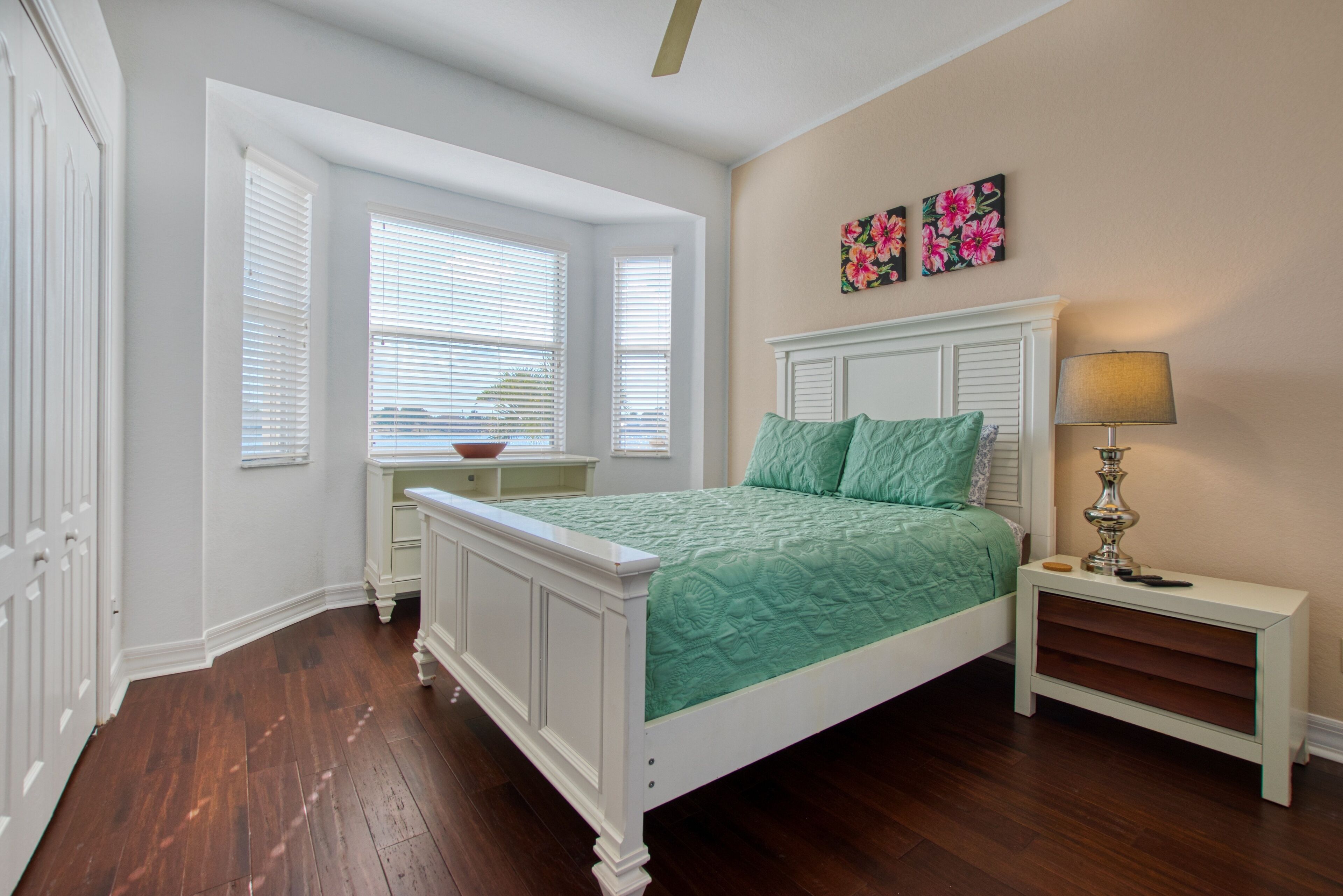 A bedroom with a bed, a nightstand, a lamp, a window with blinds, and a door.