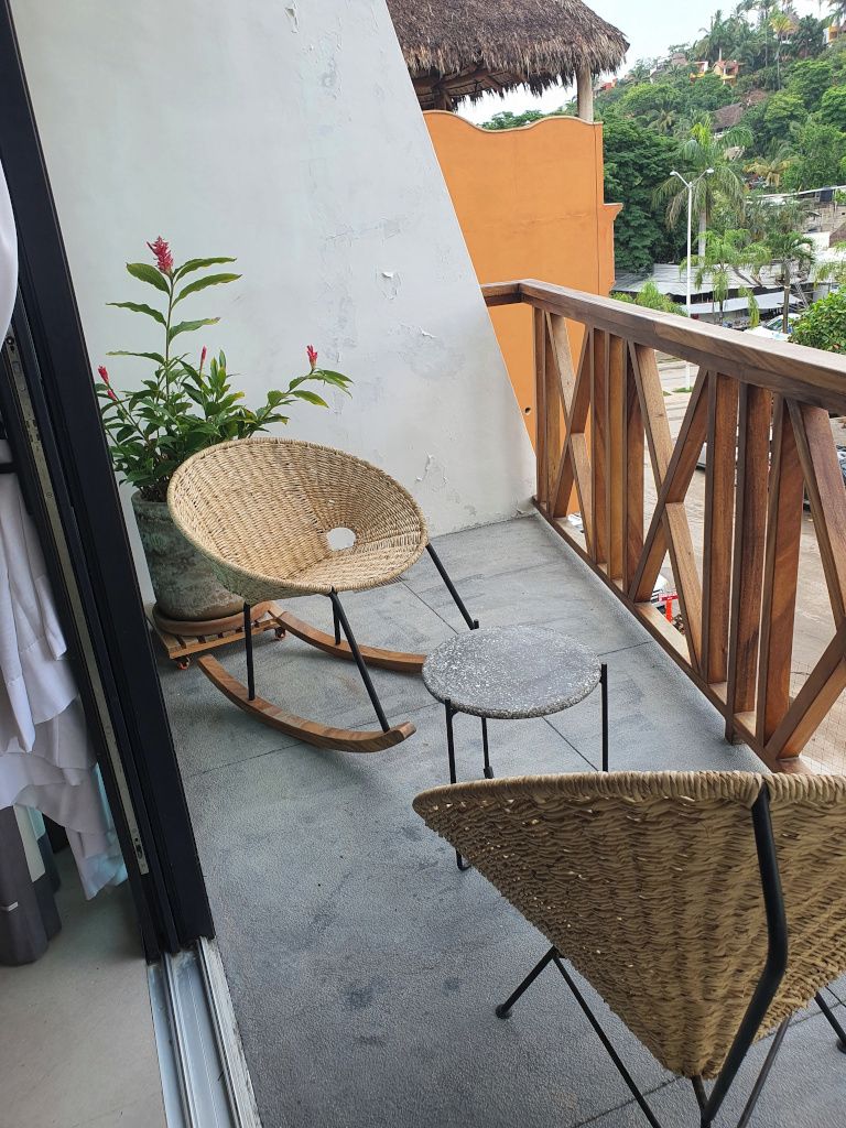 A balcony with two wicker rocking chairs, a small round table, and a potted plant with red flowers.
