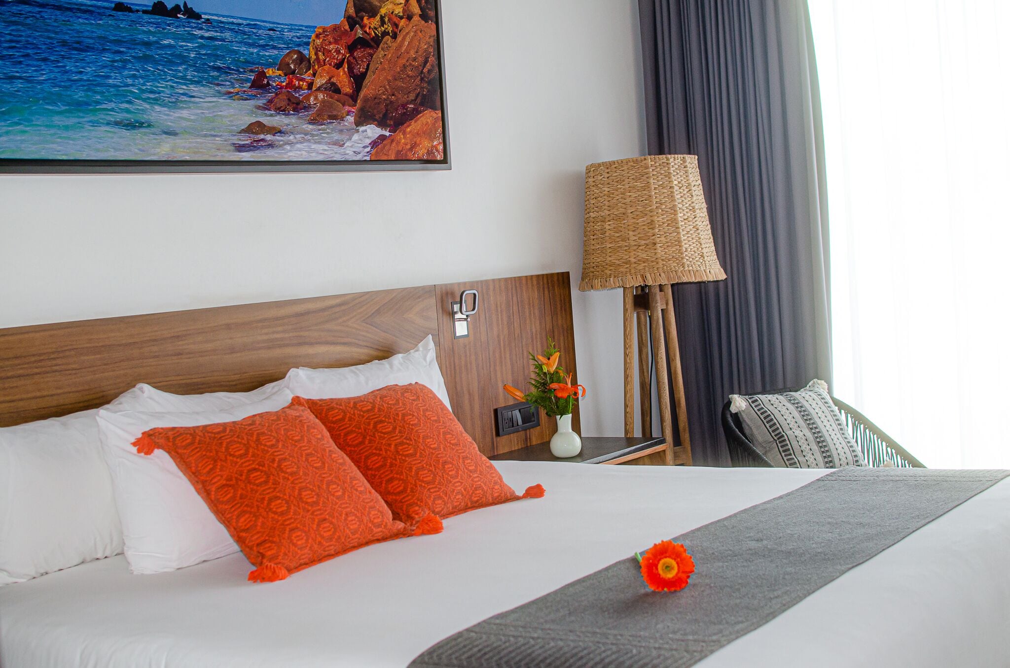 Habitación de hotel con cama, un cuadro de una playa, una lámpara y vista al mar.