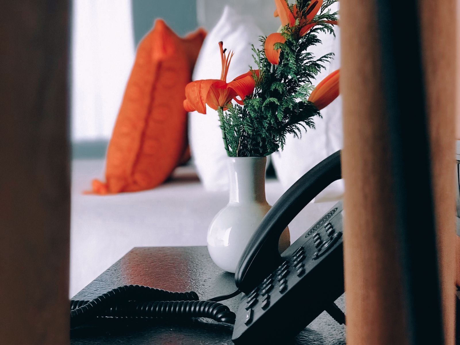 A telephone on a desk with a plant in a white vase.