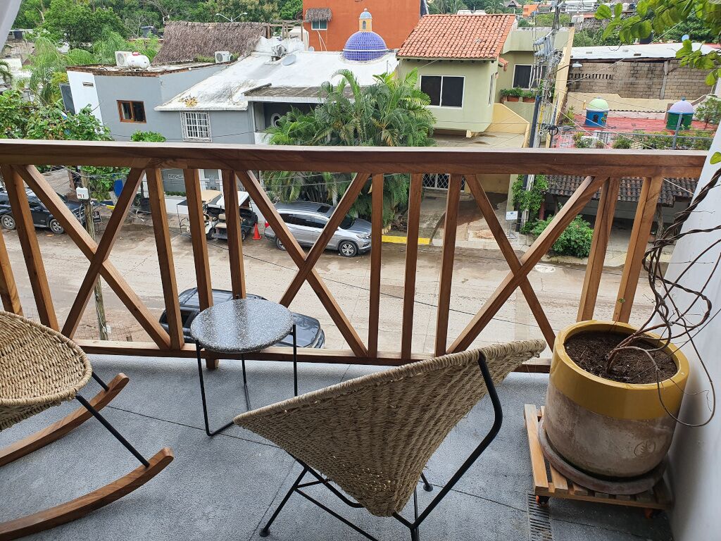 A balcony with wicker furniture, a potted plant, and a view of the street and buildings.