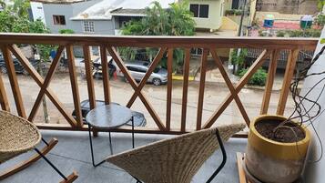 A balcony with wicker furniture, a potted plant, and a view of the street and buildings.