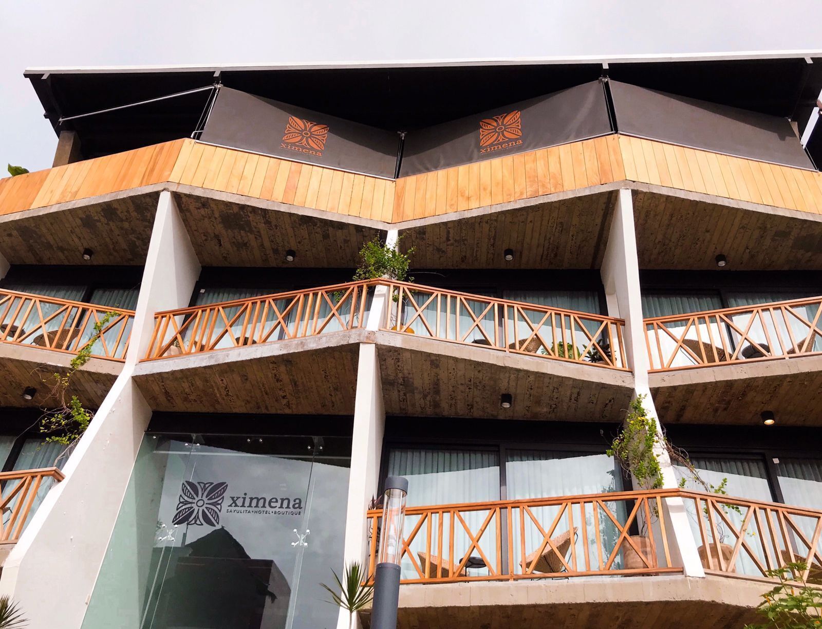 A multi-story building with a modern design, featuring balconies with wooden railings and potted plants.