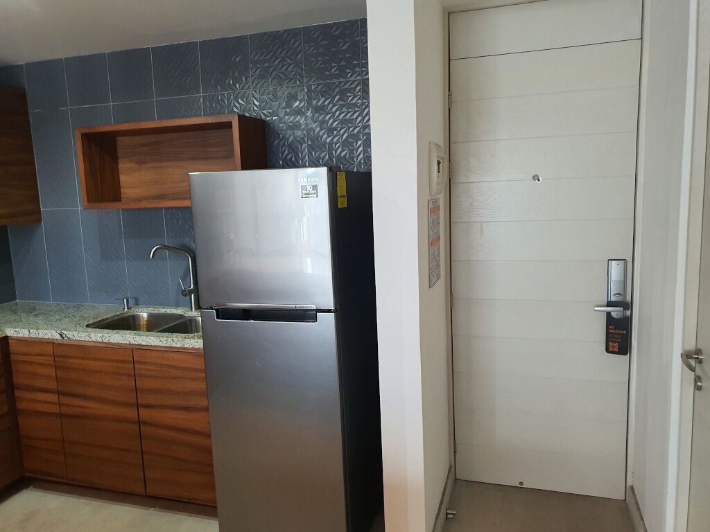 A kitchen with a stainless steel refrigerator, wooden cabinets, a granite countertop, and a blue tiled backsplash.