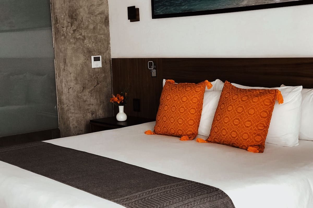 Una habitación de hotel con una cama grande, ropa blanca y almohadas con estampado naranja.