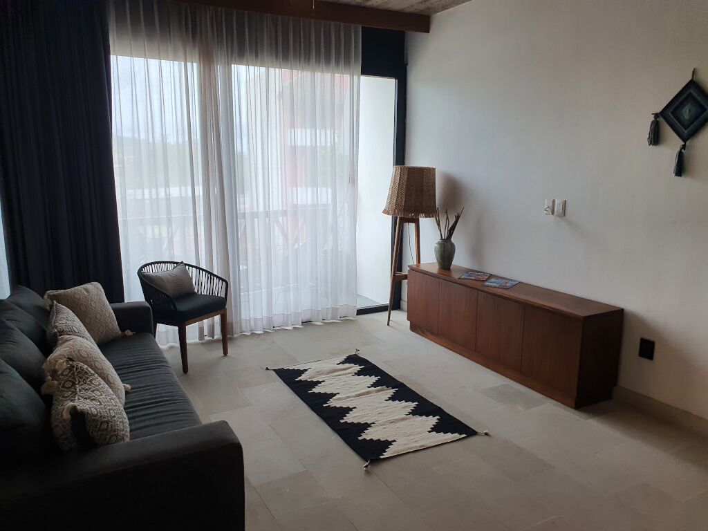 A living room with a sofa, a chair, a wooden cabinet, a lamp, and a patterned rug.
