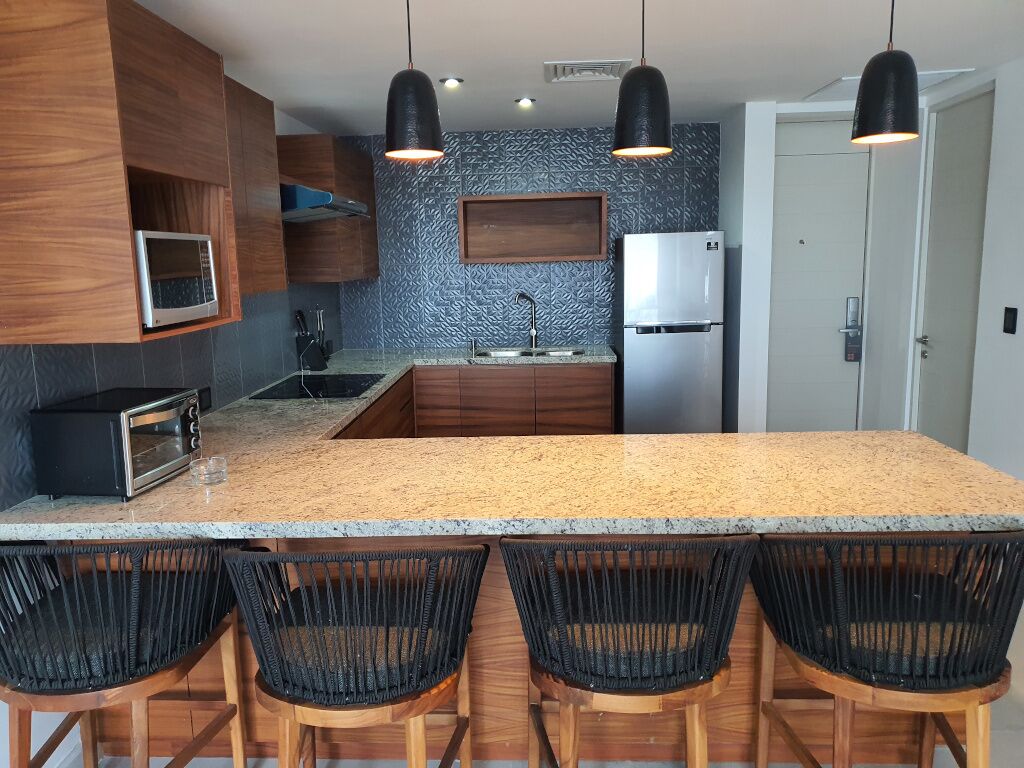 A modern kitchen with a granite countertop, built-in appliances, and black woven chairs.