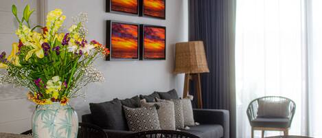 Una sala de estar con un sofá, una silla, una mesa y un florero. Cuatro cuadros enmarcados adornan la pared.