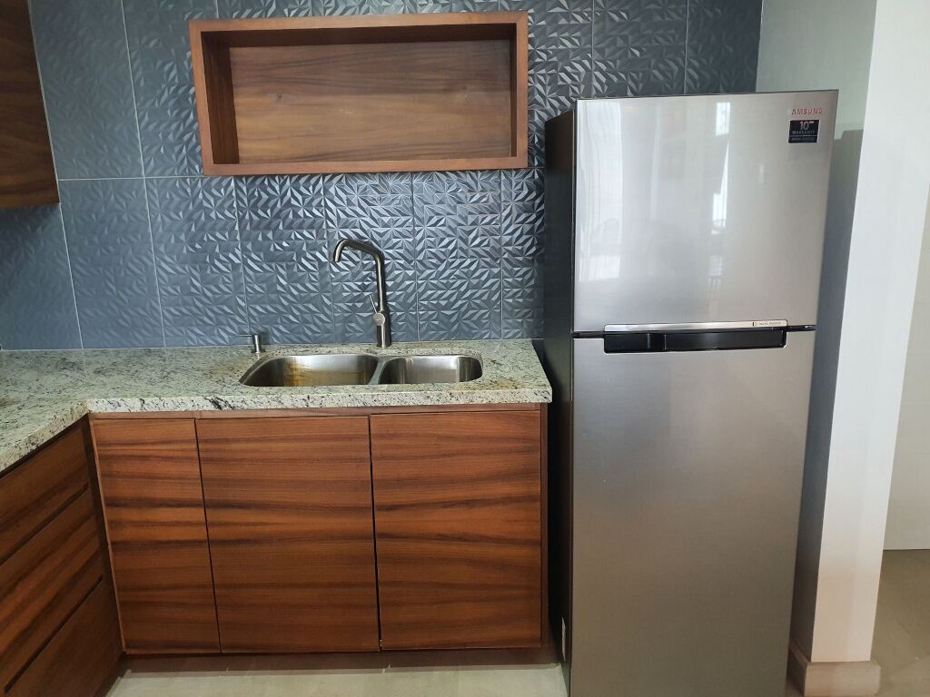 Una cocina con refrigerador de acero inoxidable, pileta doble, alacenas de madera y un salpicadero texturizado.