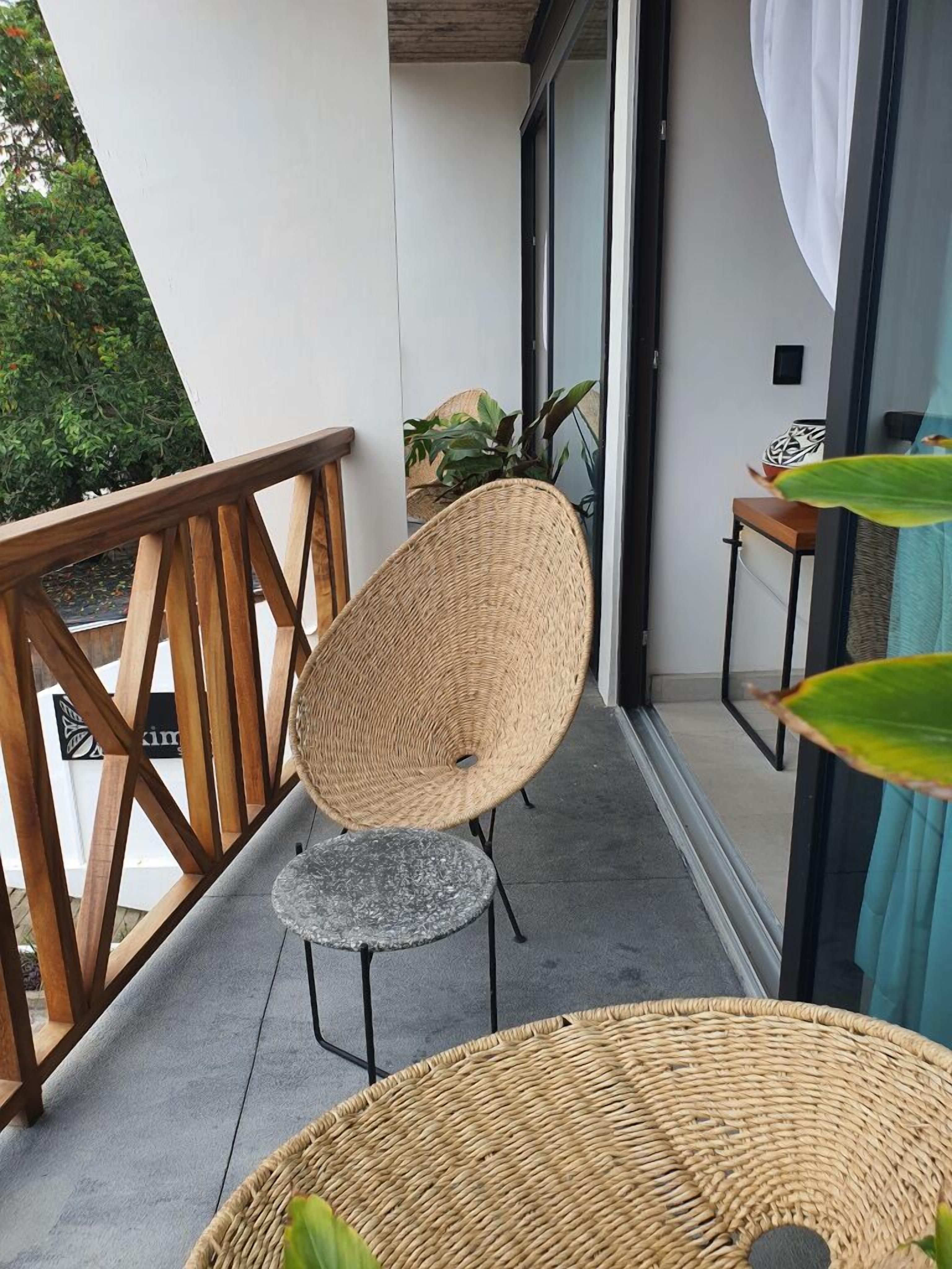A balcony with a wicker chair, a small table, and a potted plant.