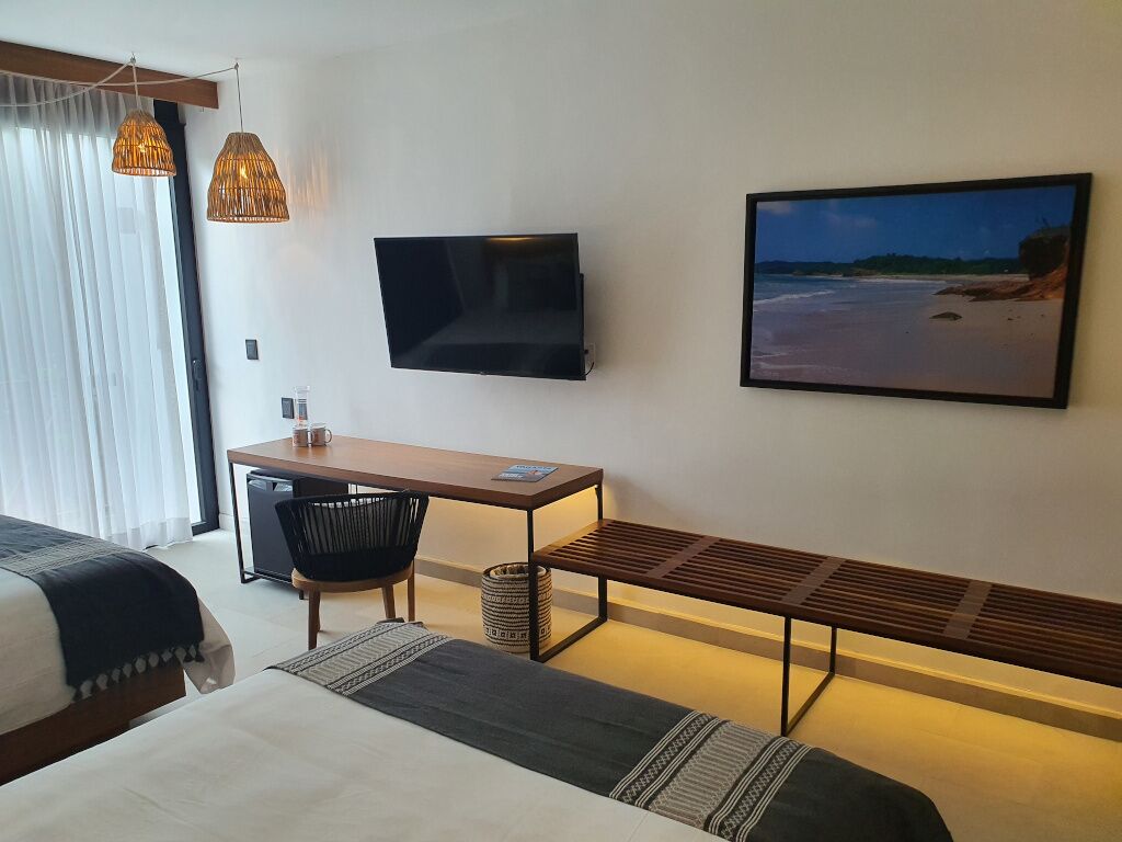 Ein Hotelzimmer mit Bett, Schreibtisch, Stuhl, Fernseher und Blick auf den Strand.