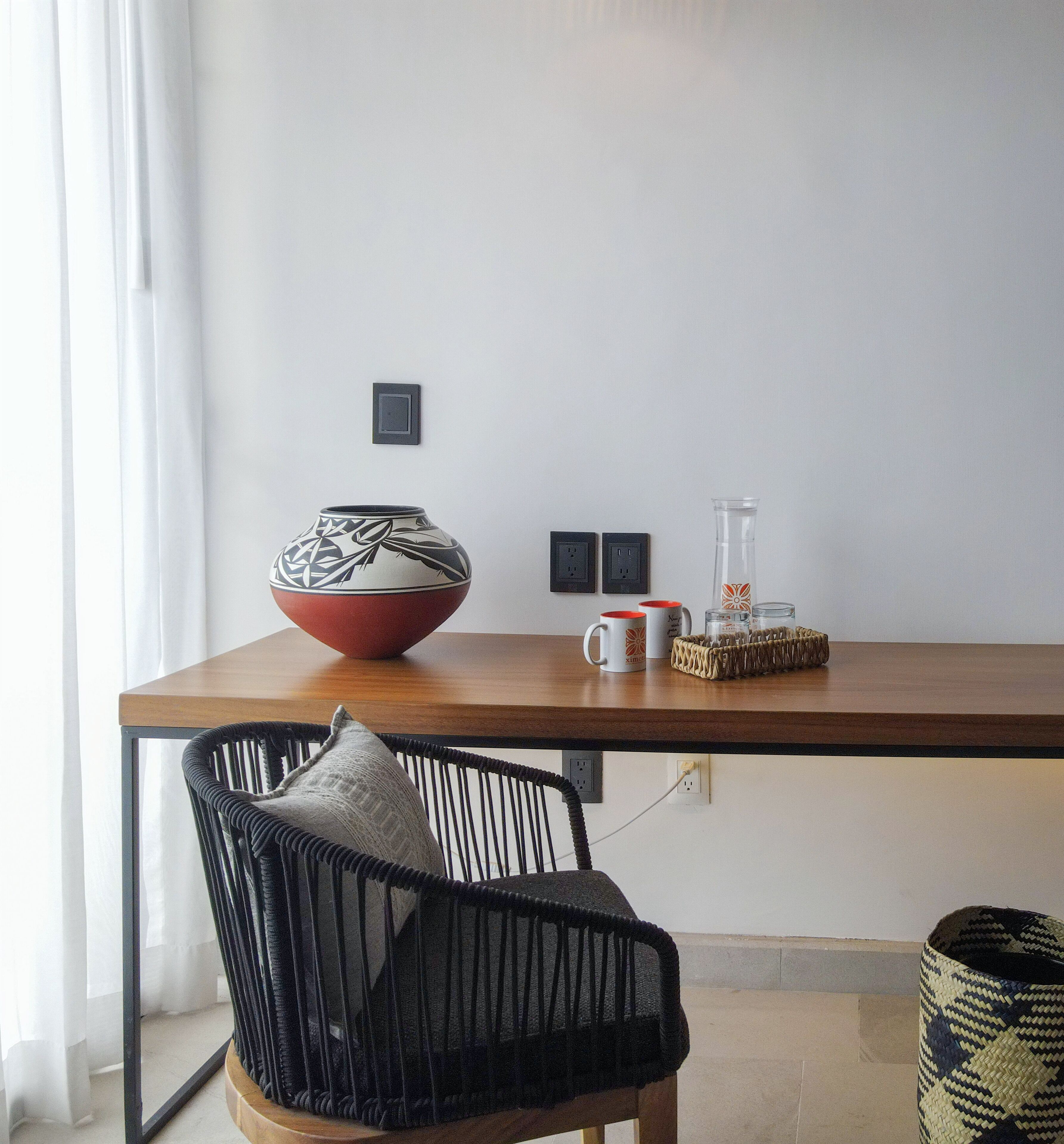 Un comedor con una mesa de madera, una cesta tejida, un florero y una silla con cojín.