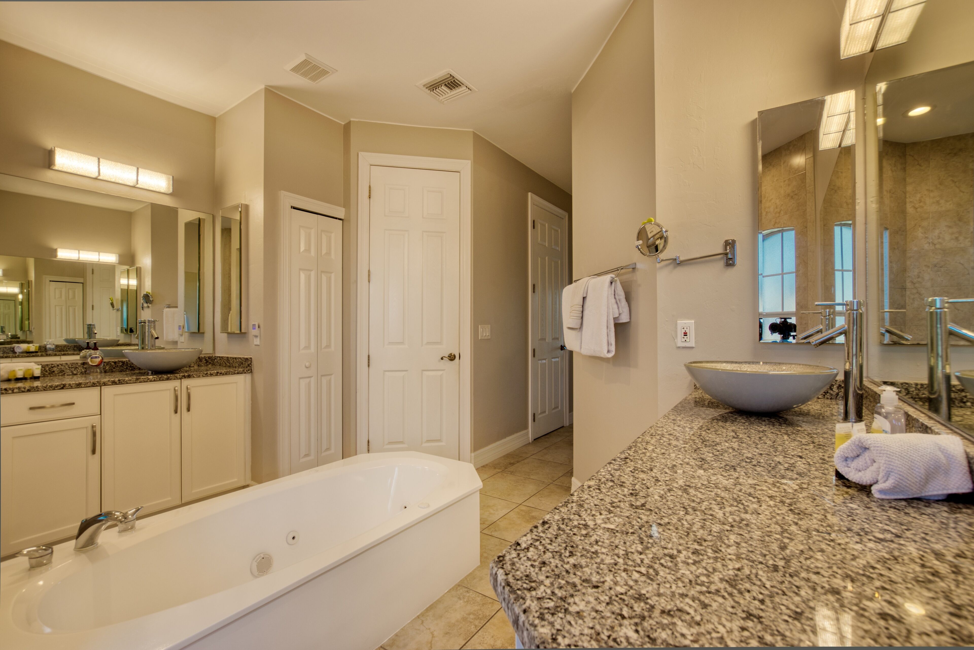 A spacious bathroom with a large bathtub, a granite countertop, and a large mirror.