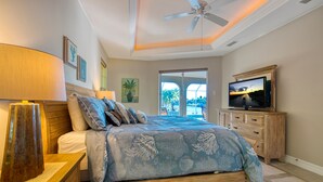 Una camera da letto con un letto, una televisione, un ventilatore a soffitto e una finestra con vista sull'esterno.