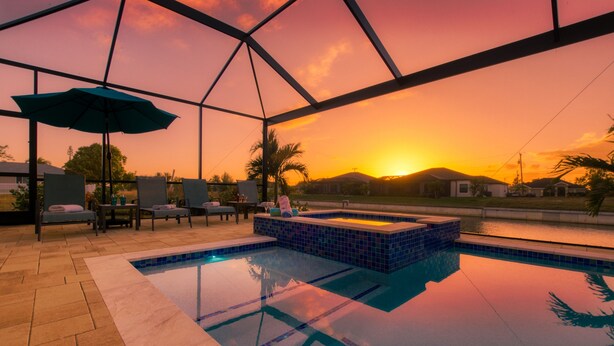 An indoor swimming pool with a glass ceiling, lounge chairs, and a view of a sunset over a body of water.