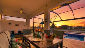 A dining area with a view of a swimming pool at sunset.