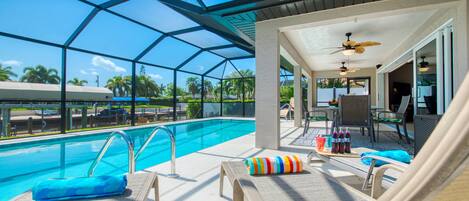 A pool area with lounge chairs, a ceiling fan, and a glass-enclosed structure.