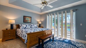 A bedroom with a bed, bedside tables, a ceiling fan, and a view through a window with curtains.
