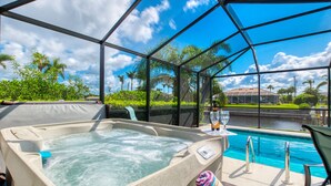 A hot tub with a glass enclosure, a pool, and a view of palm trees and a house.