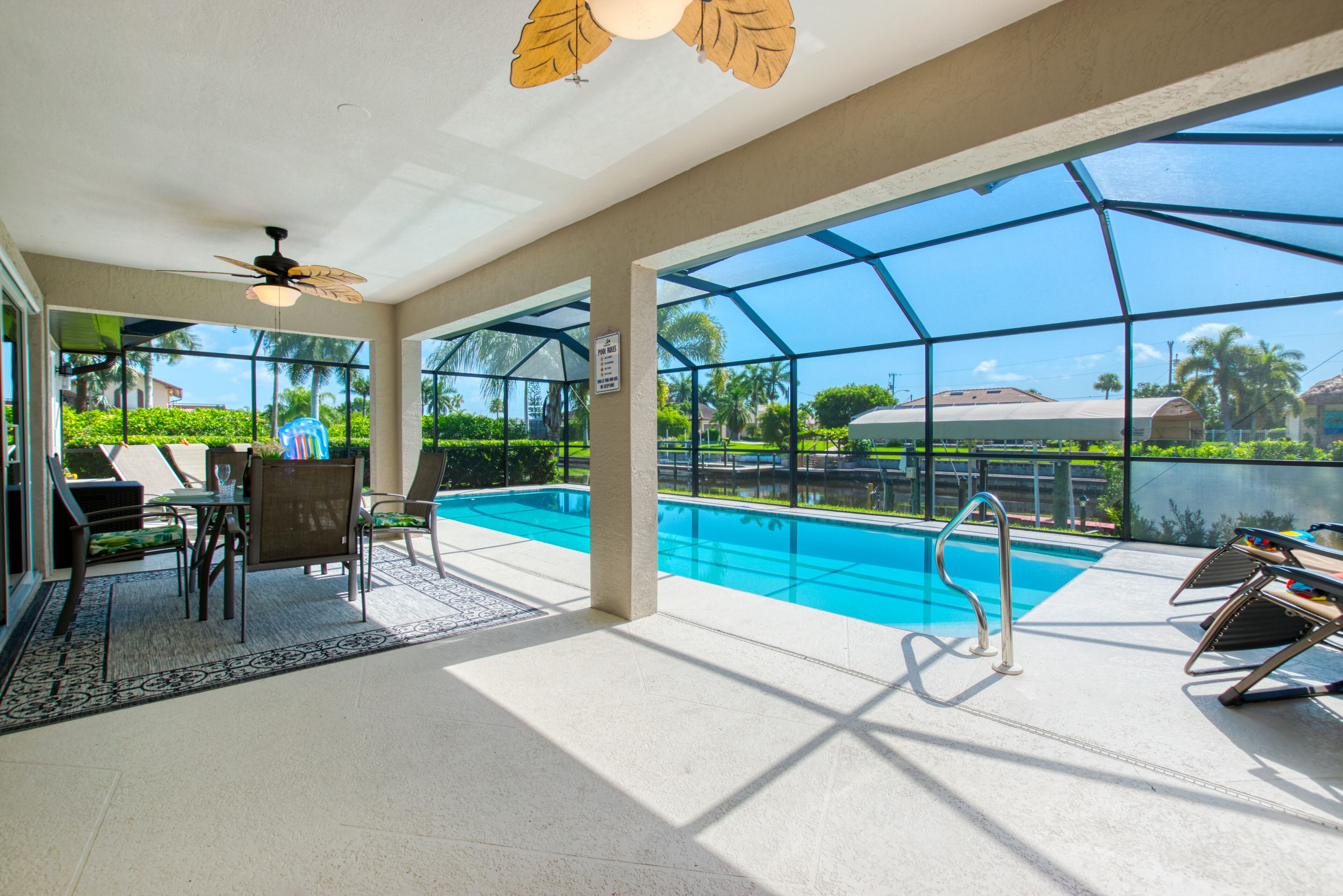 A pool area with a glass enclosure, a table with chairs, and a ceiling fan.
