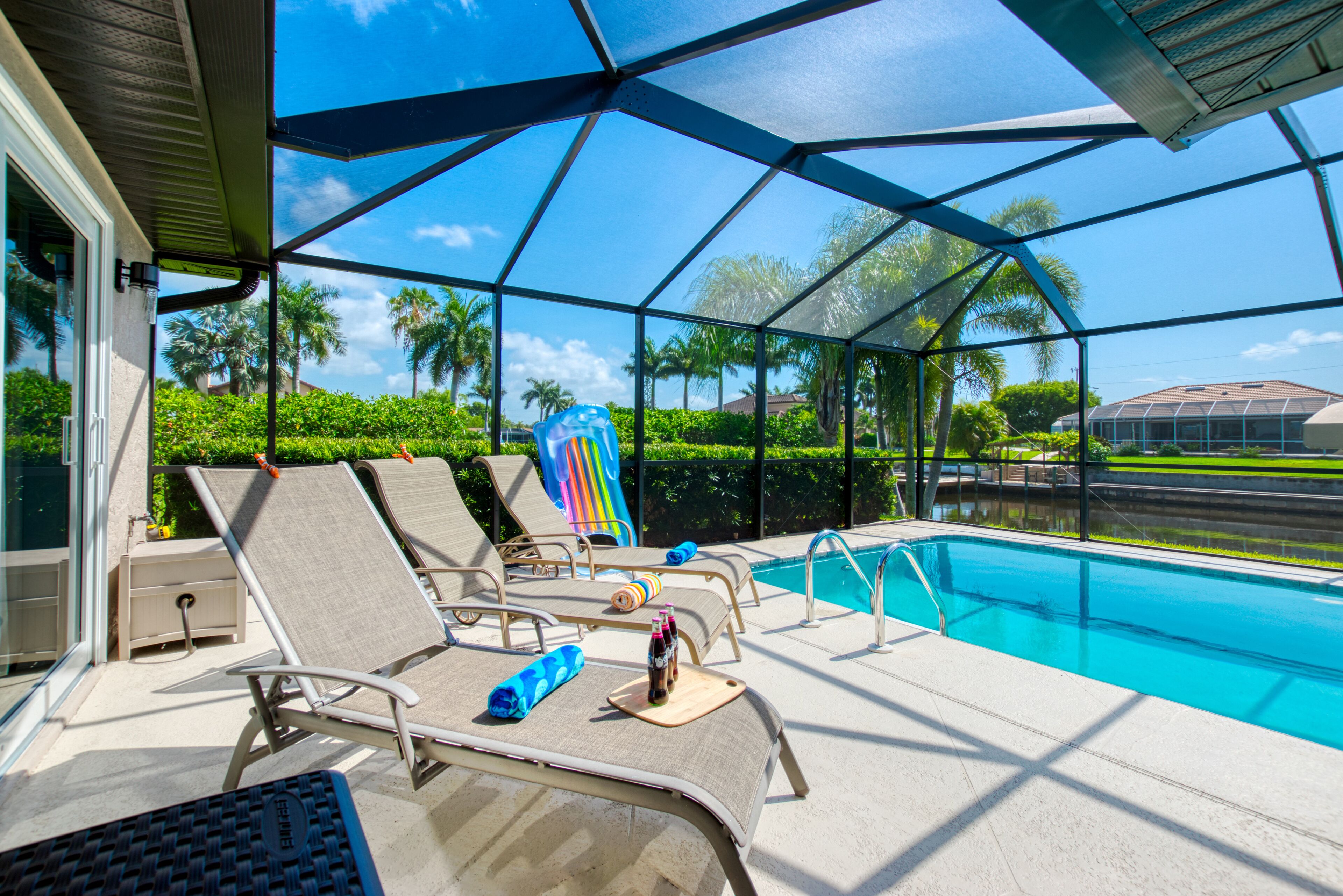 A poolside area with lounge chairs, a pool, and a view of palm trees and houses.