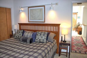 Ein Schlafzimmer mit Bett, Kopfteil, zwei Wandlampen, einem gerahmten Bild, einem Nachttisch und einem kleinen Tisch mit Lampe.