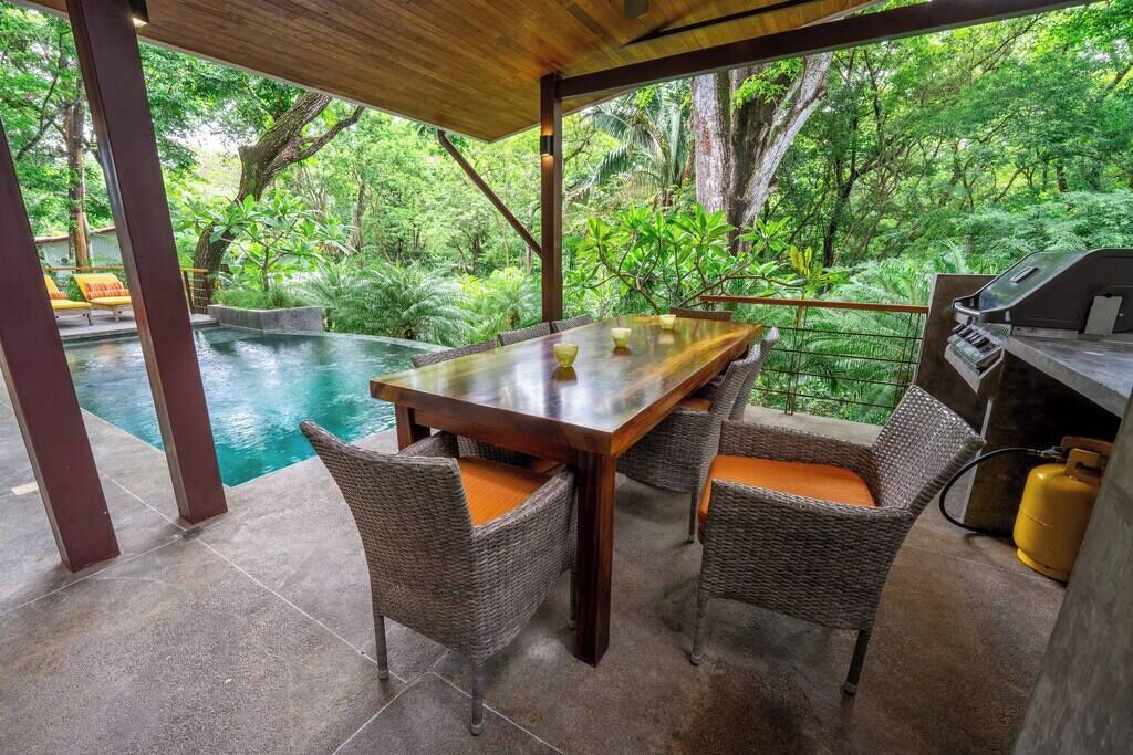 An outdoor dining area with a pool, wicker chairs, and a grill.
